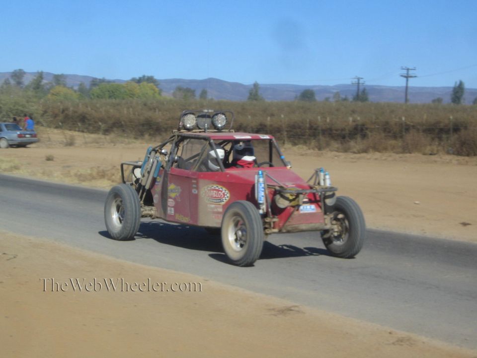 Worn red off-road race buggy with roof lights on paved desert road