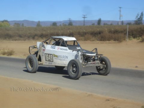 1990 Ford Bronco - white off-road race buggy numbered 1649 in Wilson Motorsports livery races along a paved desert road.