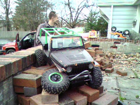 1976 GMC C/K Pickup - A remote-controlled off-road vehicle is positioned on a pile of bricks, with a man observing.