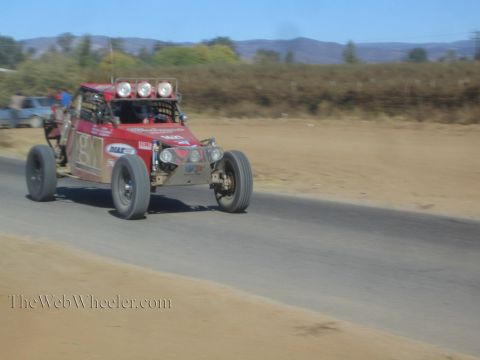 1990 Ford Bronco - red off-road race buggy with three roof lights races along a paved road, caught in motion blur.