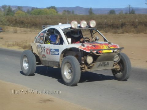 1990 Ford Bronco - white off-road race buggy numbered 513 with flame graphics and roof lights races along a paved desert road.