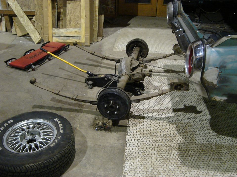 Rear axle assembly and leaf springs on floor with tire and jack