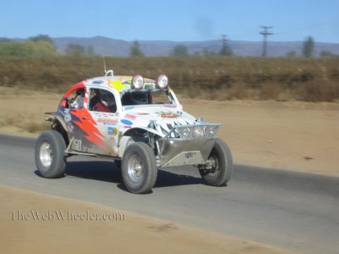 1990 Ford Bronco - white and orange Volkswagen Beetle-based race buggy numbered 50 races along a paved road in dusty desert terrain.