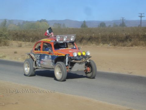 1990 Ford Bronco - orange and blue Volkswagen Beetle-based race buggy numbered 558 flies a Mexican flag along a paved desert road.