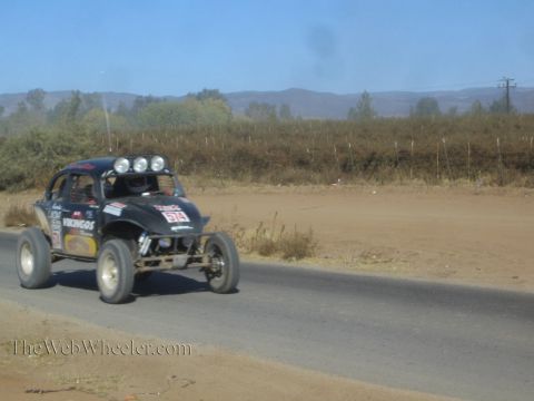 1990 Ford Bronco - black Volkswagen Beetle-based race buggy marked 514 drives along a paved road through dusty desert hills.