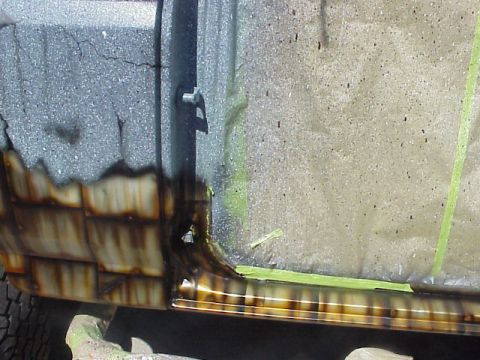 1989 Ford Bronco - The lower body panel of a vehicle shows extensive rust damage and is partially covered with green masking tape.