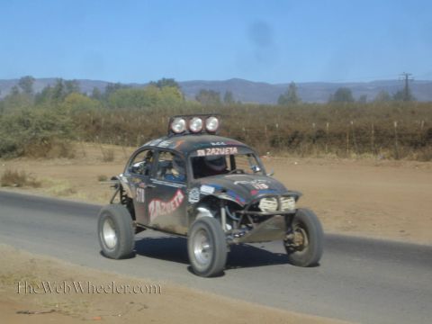 1990 Ford Bronco - black Volkswagen Beetle-based race buggy lettered Zazueta speeds along a paved road through dry desert terrain.