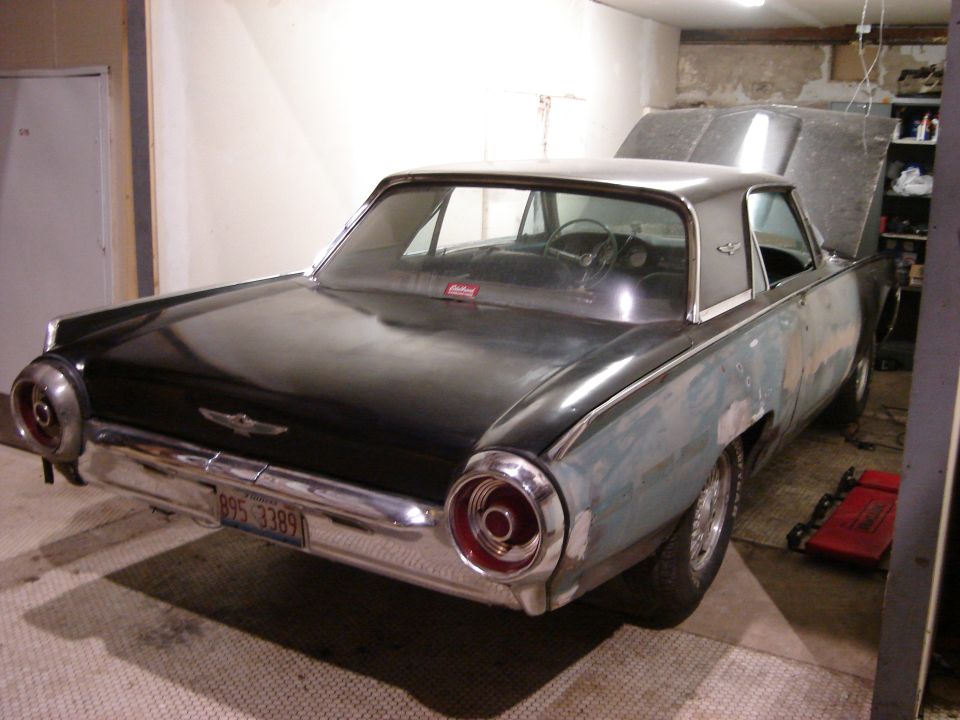Rear view of a 1961 Ford Thunderbird in a garage, hood open, primer on rear quarter panels