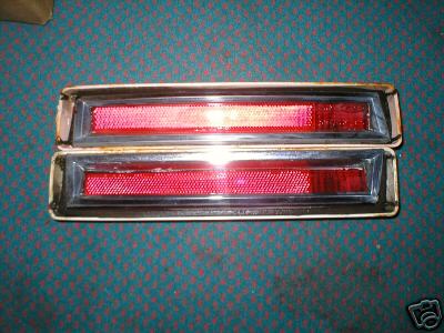 1978 Ford Mustang II - Two red taillights with chrome trim are shown against a blue carpeted background.