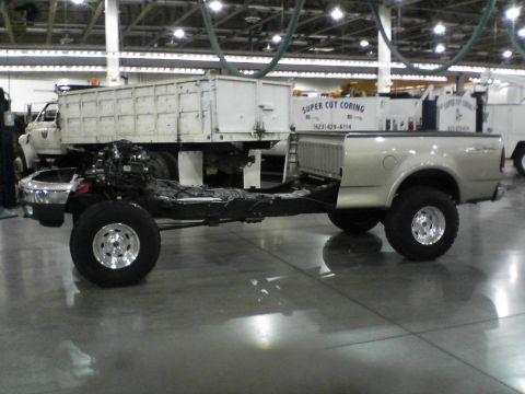 1999 Ford F-150 - A pickup truck's chassis and engine are visible, with the bed attached, next to a large dump truck.