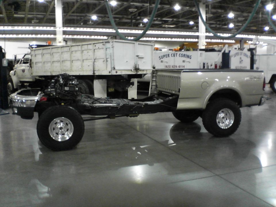 Pickup truck chassis with engine and body, parked next to a dump truck. The truck bed is attached