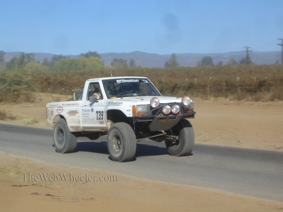White off-road race pickup numbered 739 mid-jump on a paved desert road