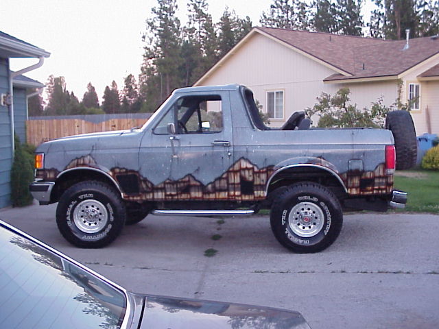 Lifted gray Ford Bronco, topless, with mountain mural, side view on driveway