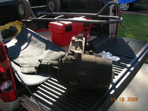 1985 Ford Bronco - A transfer case is loaded into the back of a truck, alongside other equipment.