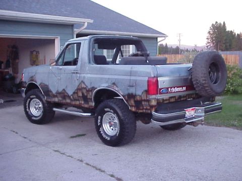 1989 Ford Bronco - Lifted grey full-size Ford Bronco with the removable top off, photographed from the rear-left three-quarter in a residential driveway. It w…