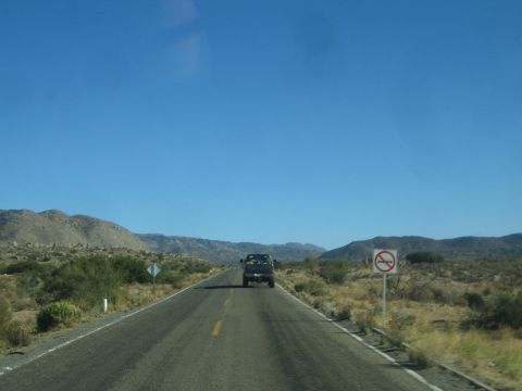 1990 Ford Bronco - desert two-lane highway photographed through a windshield, with a dark truck ahead and a road sign on the right.