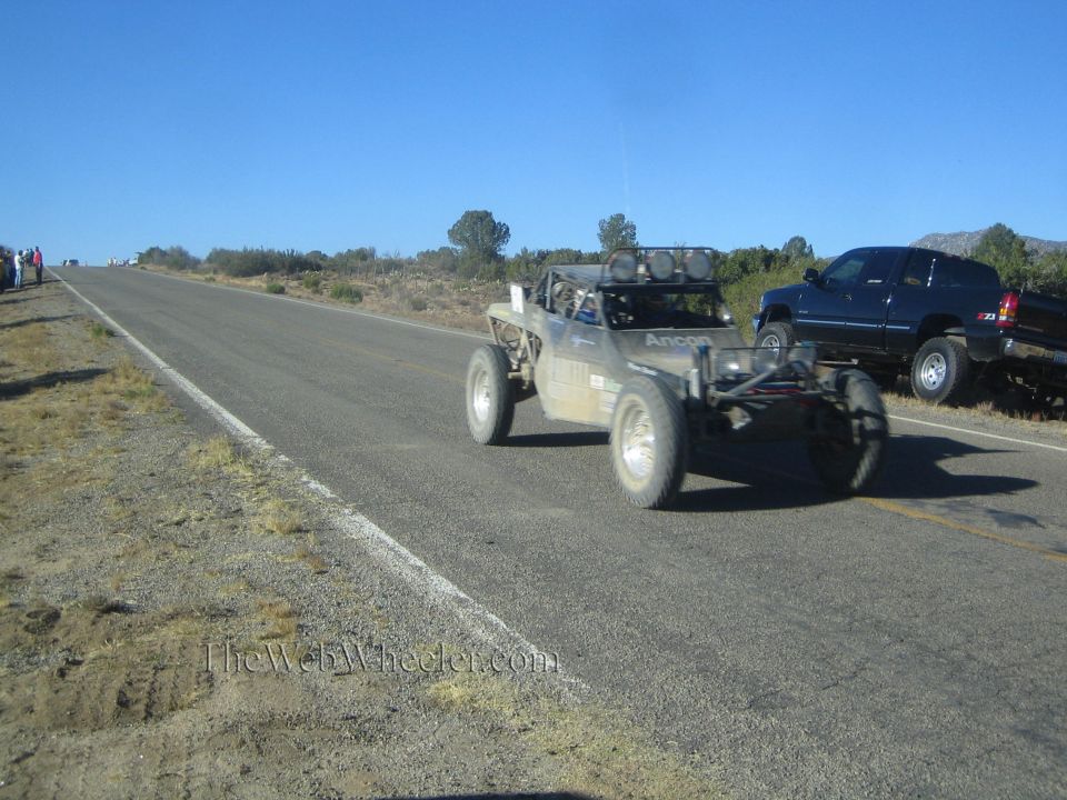 Tan single-seat off-road race buggy on rural road beside a dark SUV