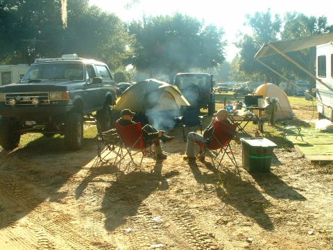 1995 Ford Bronco - A group enjoys a campfire at a campsite with several vehicles and tents visible.