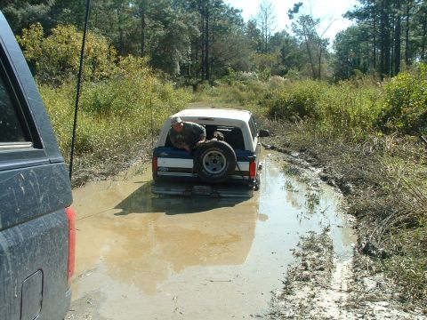 1995 Ford Bronco - A man sits in the back of a Ford Bronco that is stuck in a muddy trail surrounded by trees.