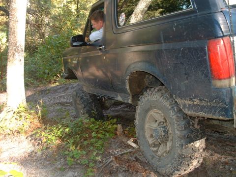 1995 Ford Bronco - 1995 Ford Bronco navigating a muddy trail with a driver behind the wheel.