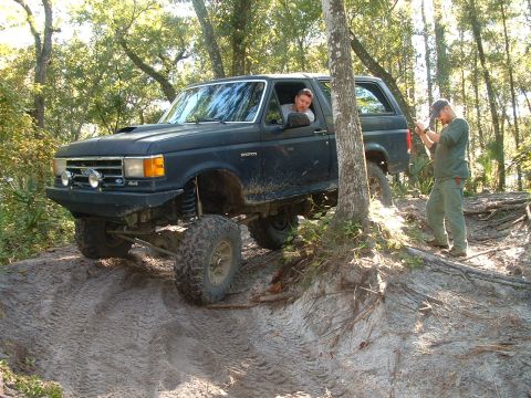 1995 Ford Bronco - A black Ford Bronco navigates a challenging off-road course with two people present.