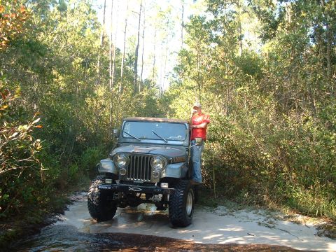 1995 Ford Bronco - A man stands next to a Jeep CJ-7 on a muddy, wooded trail.