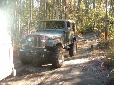1995 Ford Bronco - Off-road Jeep CJ-7 Laredo navigating a muddy trail through a wooded area.