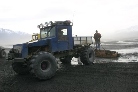 2003 Jeep TJ - A large blue off-road truck tows a derelict vehicle across a muddy plain with mountains in the background.