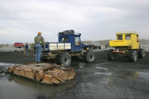 2003 Jeep TJ - Several large off-road vehicles are present in a muddy, outdoor environment with a submerged vehicle chassis in the foreground.