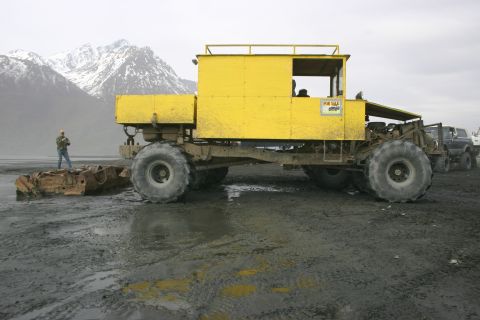 2003 Jeep TJ - A unique, custom-built vehicle with oversized tires sits on a muddy terrain, with snow-capped mountains in the background.