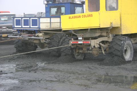 2003 Jeep TJ - A large, multi-wheeled vehicle with "ALASKAN COLORS" painted on its side is seen stuck in thick mud.