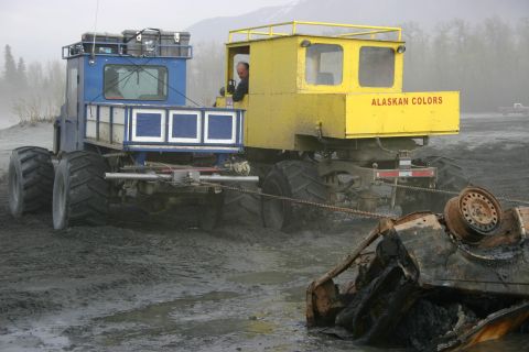 2003 Jeep TJ - An off-road truck tows a heavily damaged and burnt vehicle from a muddy area, with another truck assisting.