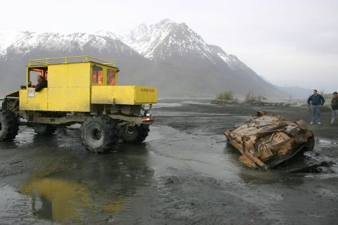 2003 Jeep TJ - A yellow truck is parked near a heavily damaged vehicle in a muddy, outdoor scene with mountains in the background.