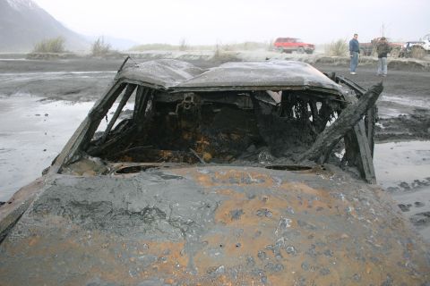2003 Jeep TJ - A heavily damaged and mud-covered vehicle sits in a desolate, muddy landscape with other vehicles in the distance.