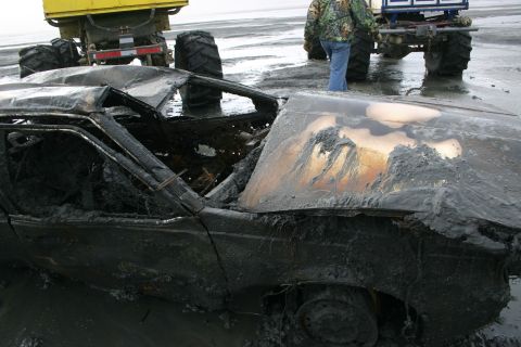 2003 Jeep TJ - A heavily damaged and burnt car sits on muddy terrain, with two tractors visible behind it.