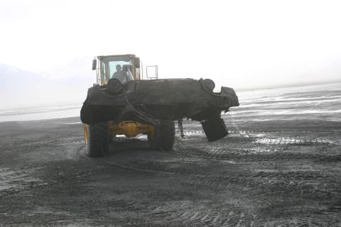 2003 Jeep TJ - A yellow loader lifts a severely damaged vehicle on a desolate, wet, sandy area with mountains in the background.
