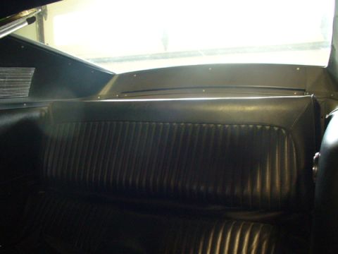 1968 Ford Mustang - The ribbed black vinyl rear seat of a classic car is shown from the back, with a bright window in the background.