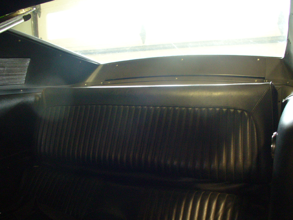 Rear bench seat in a car, black vinyl with vertical pleats. Top of seatback has a curved shape