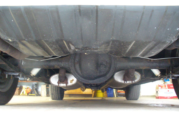 Underside rear view of vehicle showing rear axle, differential, and dual chrome exhaust tips on a lift.