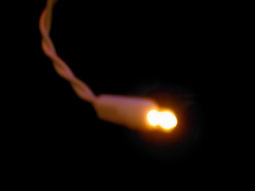 Close-up of a single illuminated Christmas light with a twisted cord against a black background