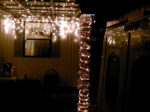 side of a vehicle covered in Christmas lights, parked next to a house with lights and a window