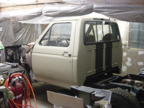 1991 Ford Bronco - This 1991 Ford Bronco cab is undergoing chassis reassembly, showing its beige exterior with distinctive black stripes.