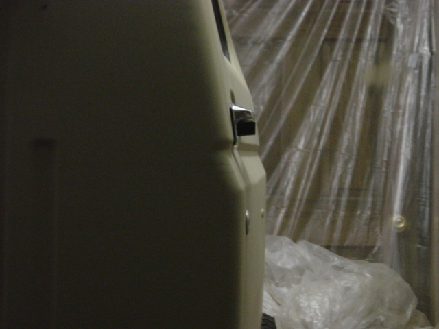 Side view of beige SUV door handle and panel, plastic sheeting in background