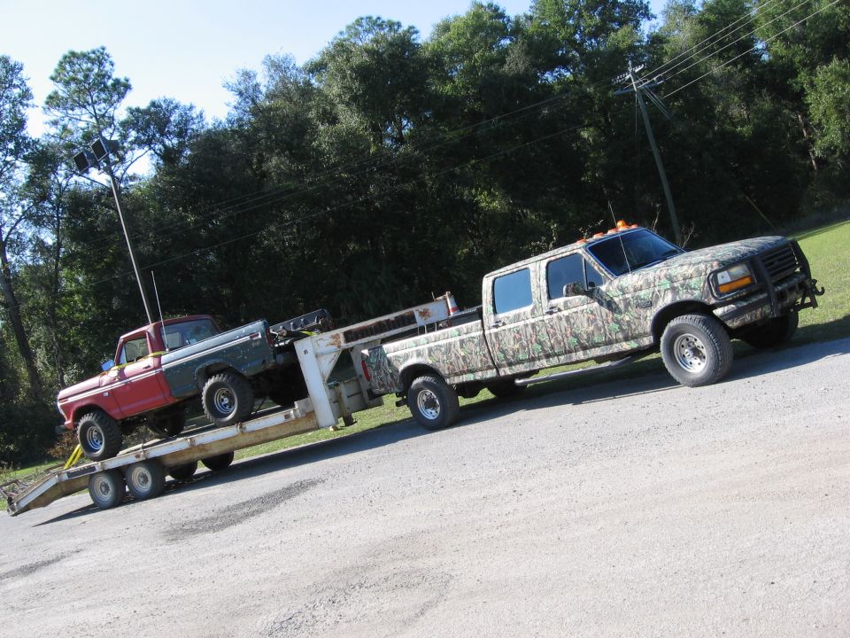 camo-wrapped truck is towing a trailer with a red and green pickup on it