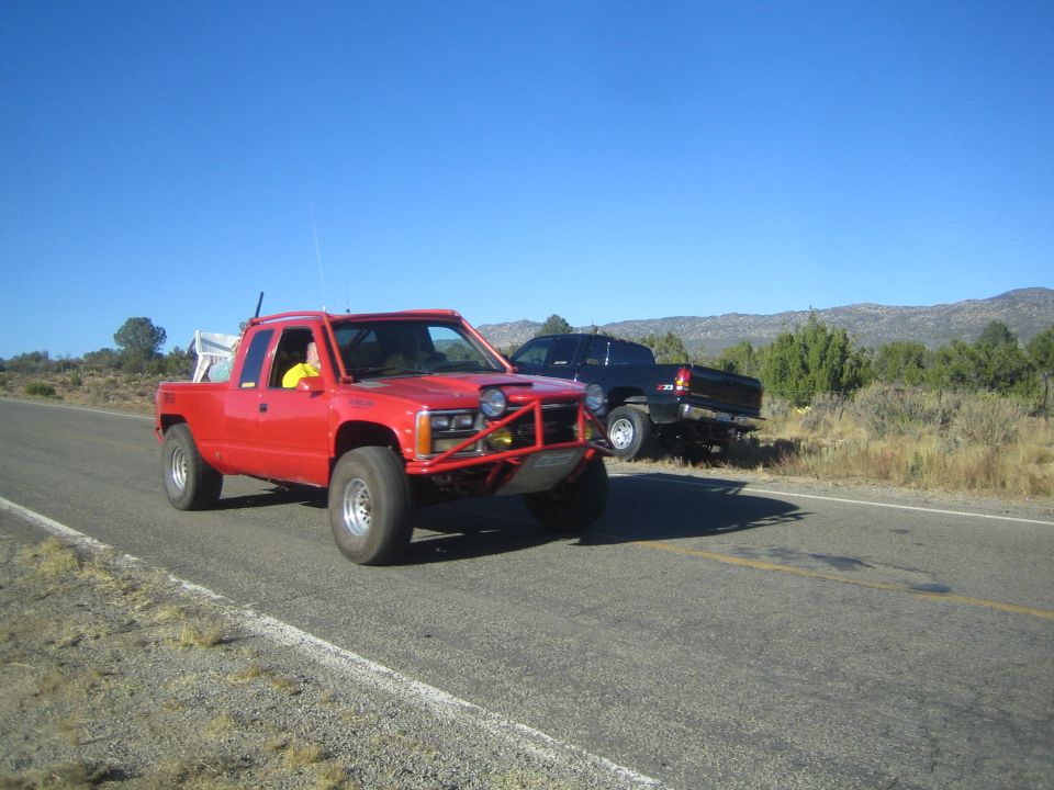 Red extended-cab pickup truck on rural highway with parked dark truck