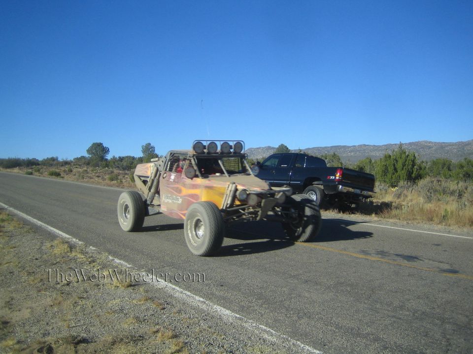 Flame-painted off-road race buggy on rural highway with parked pickup