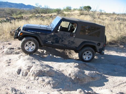 2005 Jeep YJ - This Jeep Wrangler Rubicon is navigating a rocky, off-road trail under a clear sky.