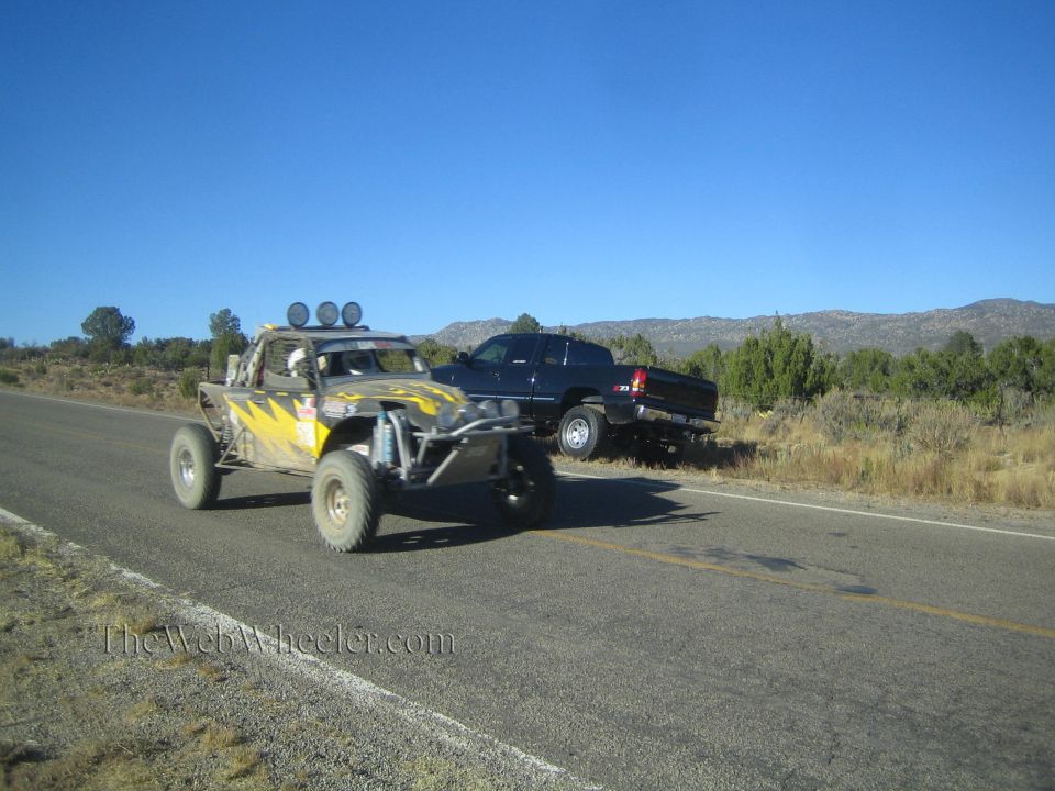 Black and yellow off-road race buggy on rural highway with parked pickup