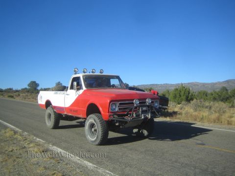 1990 Ford Bronco - vintage red and white Chevrolet pickup with a winch and front light bar drives a rural highway in hilly terrain.