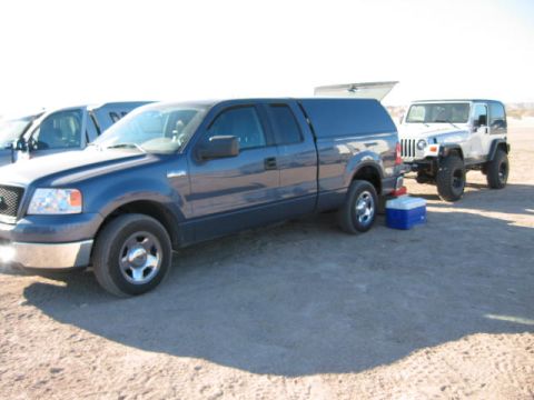 1997 Ford Ranger - Blue pickup truck and white Jeep Wrangler parked on dirt ground.